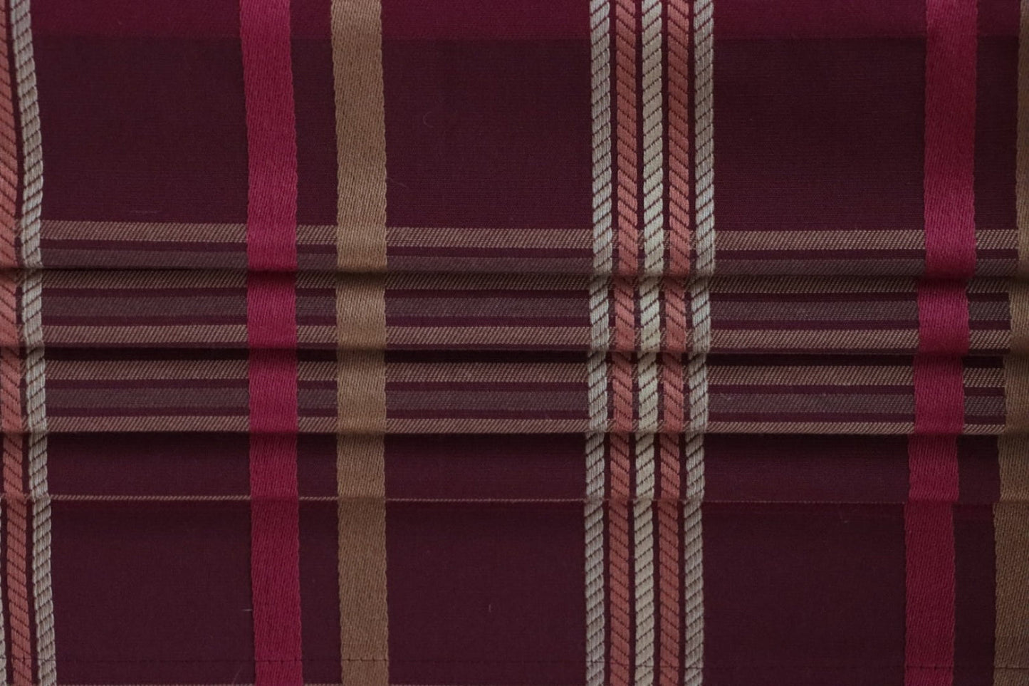 Braxton Check Burgundy fabric by Arte Fresca Outlet folded like a Roman blind, illustrating its structured appearance and the classic plaid pattern in deep burgundy, gold, and rose, perfect for window treatments.