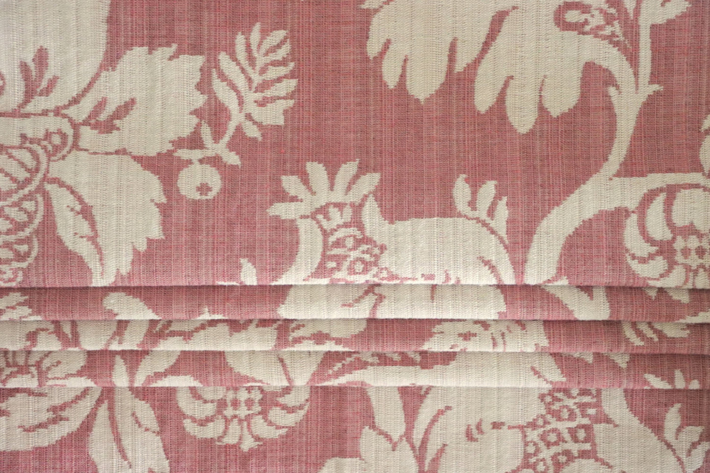 MARY ROSE jacquard fabric from Arte Fresca Outlet folded compactly like a window blind, emphasizing its refined woven texture and the prominent creamy white floral pattern on old rose. This versatile jacquard is suitable for elegant roller blinds and decorative projects, offering a touch of classic, romantic beauty.