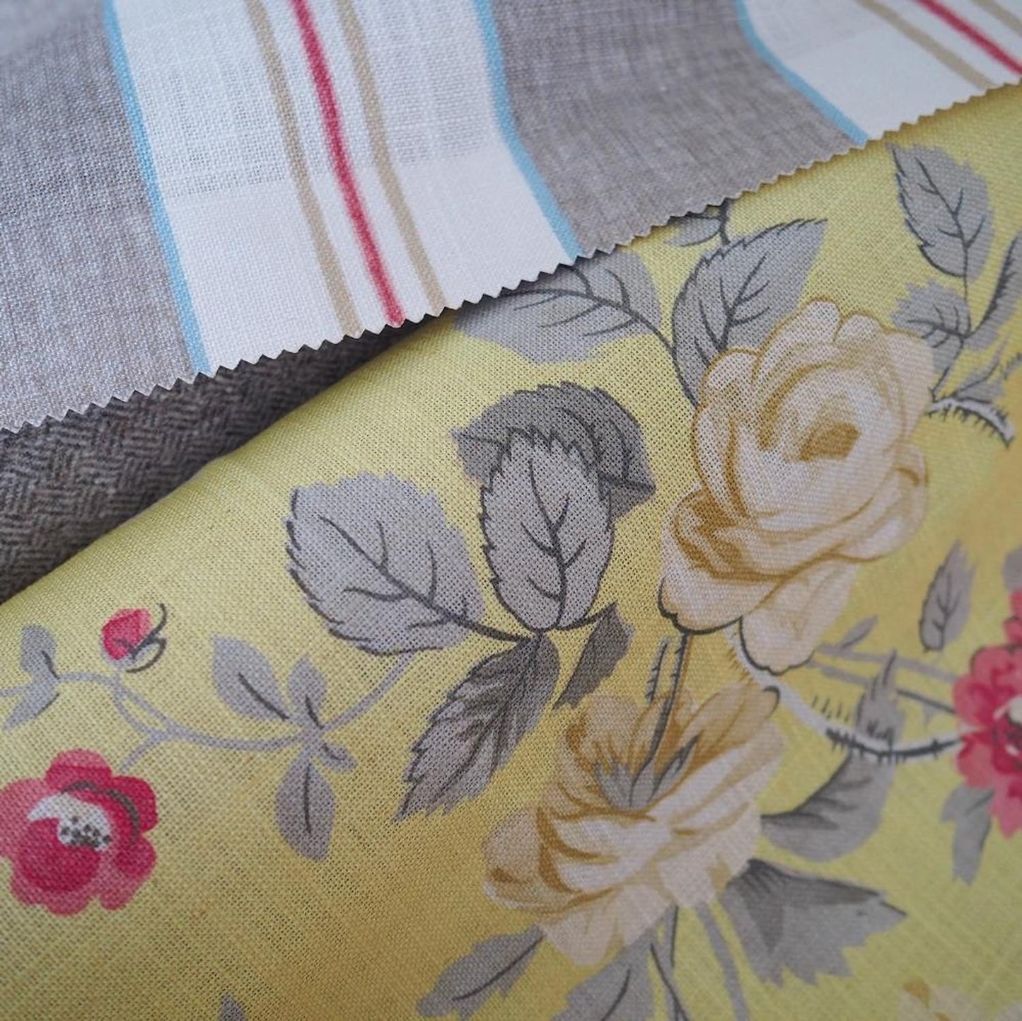 Close-up of PHILIPPA CAMOMILE fabric from Arte Fresca Outlet, revealing the detailed floral rose motifs in cream-white and red, subtle leaf vein drawing, and the distinct linen-like texture on its soft yellow ground, characteristic of this printed design.