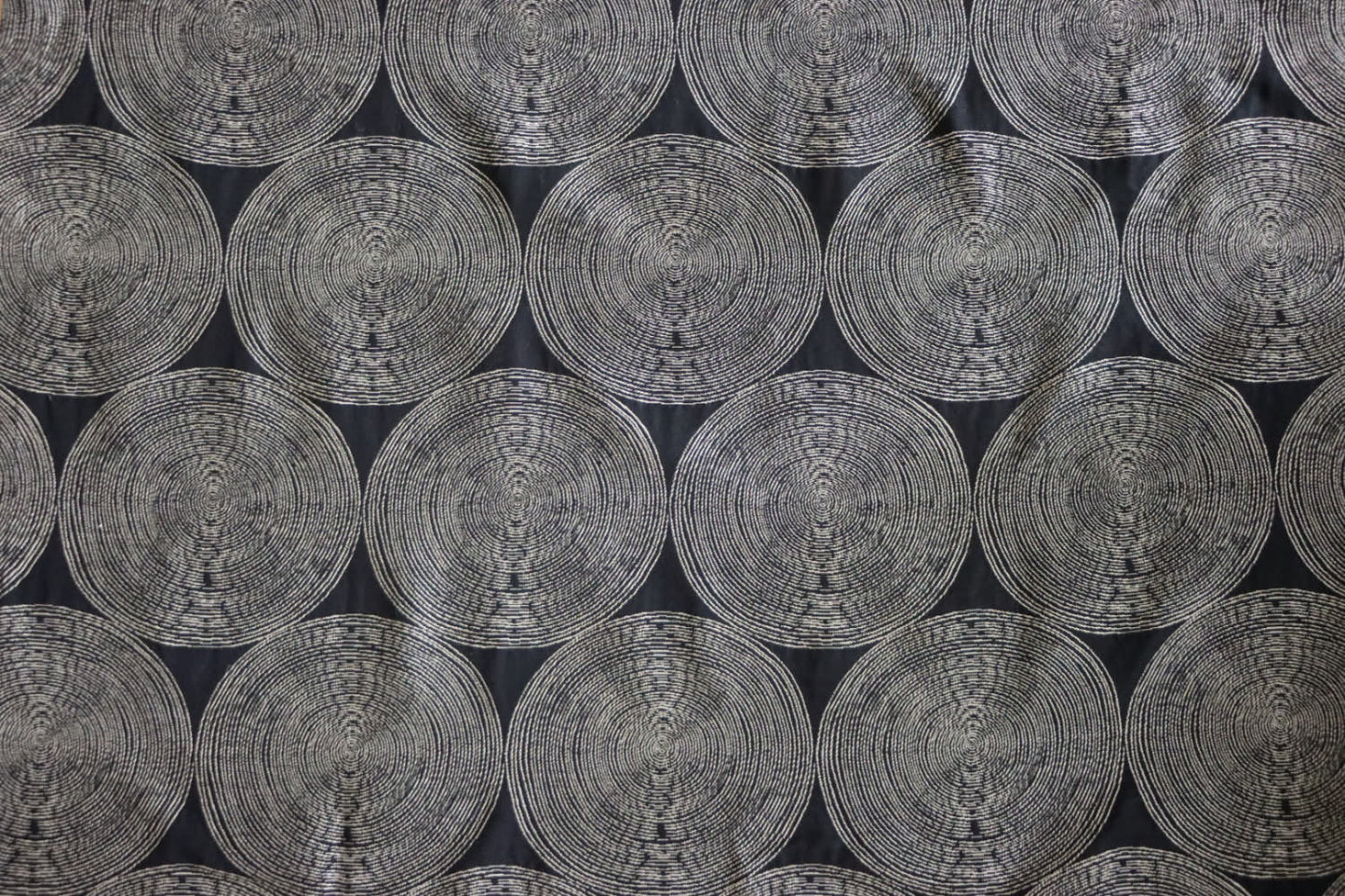 A close-up view of the Adam Black fabric by Arte Fresca Outlet, showcasing its deep black background with rhythmic, overlapping concentric circles in light cream and beige tones. The woven texture within the circles adds depth to this modern, graphic design.