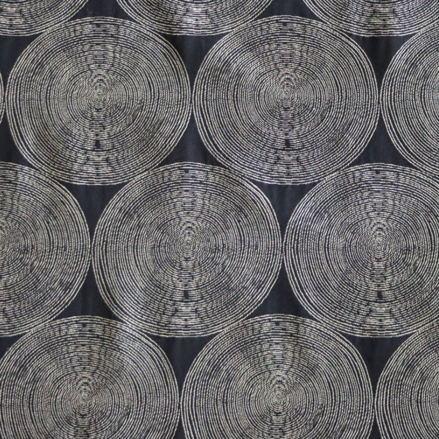 A close-up view of the Adam Black fabric by Arte Fresca Outlet, showcasing its deep black background with rhythmic, overlapping concentric circles in light cream and beige tones. The woven texture within the circles adds depth to this modern, graphic design.