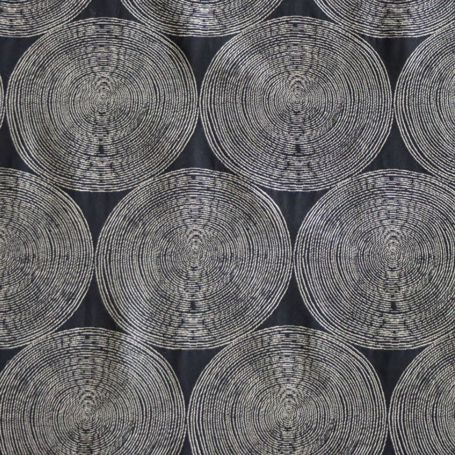 A close-up view of the Adam Black fabric by Arte Fresca Outlet, showcasing its deep black background with rhythmic, overlapping concentric circles in light cream and beige tones. The woven texture within the circles adds depth to this modern, graphic design.