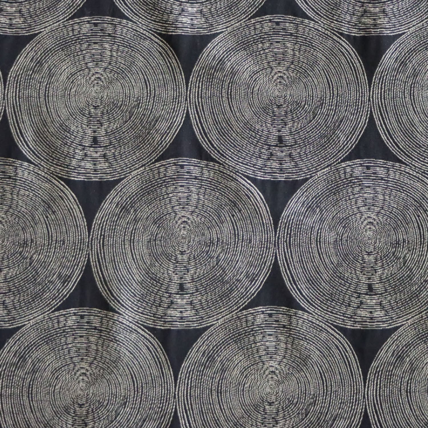 A close-up view of the Adam Black fabric by Arte Fresca Outlet, showcasing its deep black background with rhythmic, overlapping concentric circles in light cream and beige tones. The woven texture within the circles adds depth to this modern, graphic design.