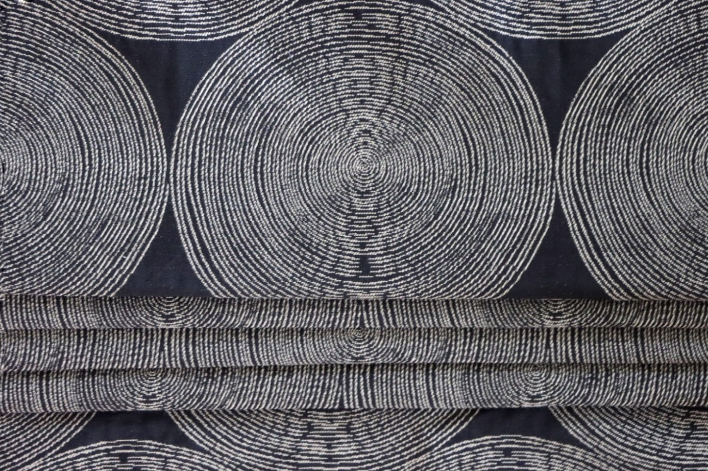 The Adam Black fabric by Arte Fresca Outlet arranged in neat folds, mimicking a roller blind, showcasing its crisp lines and how the striking pattern of light circles on a dark black woven background creates a bold, modern statement.
