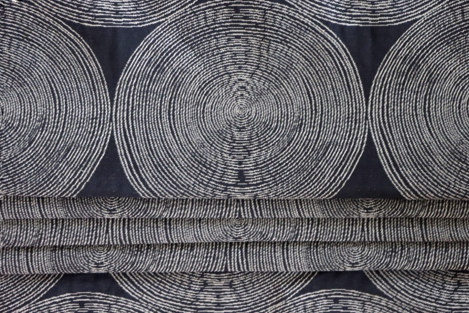 The Adam Black fabric by Arte Fresca Outlet arranged in neat folds, mimicking a roller blind, showcasing its crisp lines and how the striking pattern of light circles on a dark black woven background creates a bold, modern statement.