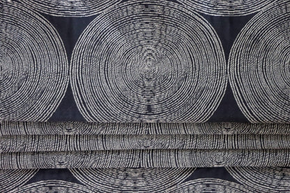 The Adam Black fabric by Arte Fresca Outlet arranged in neat folds, mimicking a roller blind, showcasing its crisp lines and how the striking pattern of light circles on a dark black woven background creates a bold, modern statement.
