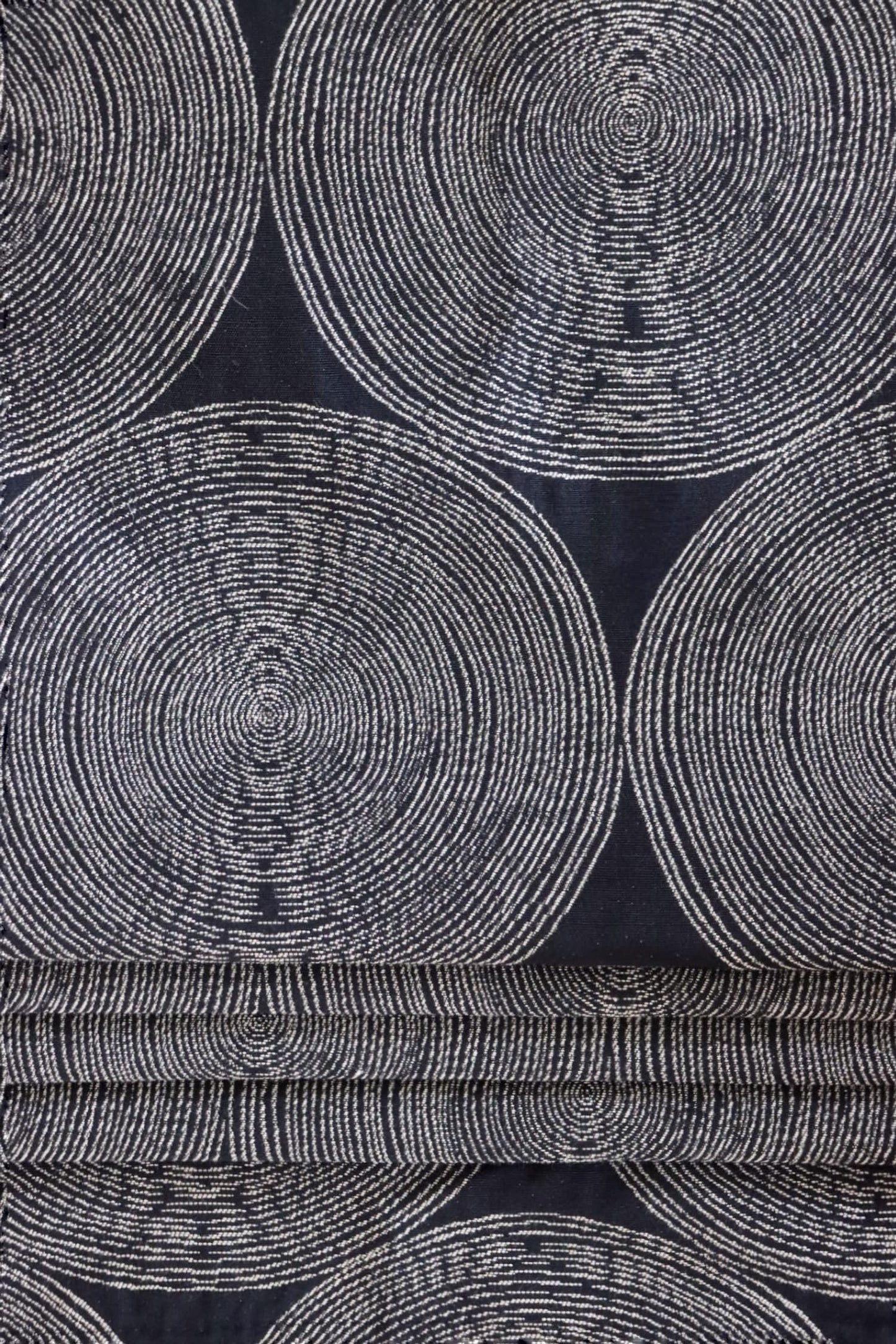 The Adam Black fabric by Arte Fresca Outlet arranged in neat folds, mimicking a roller blind, showcasing its crisp lines and how the striking pattern of light circles on a dark black woven background creates a bold, modern statement.