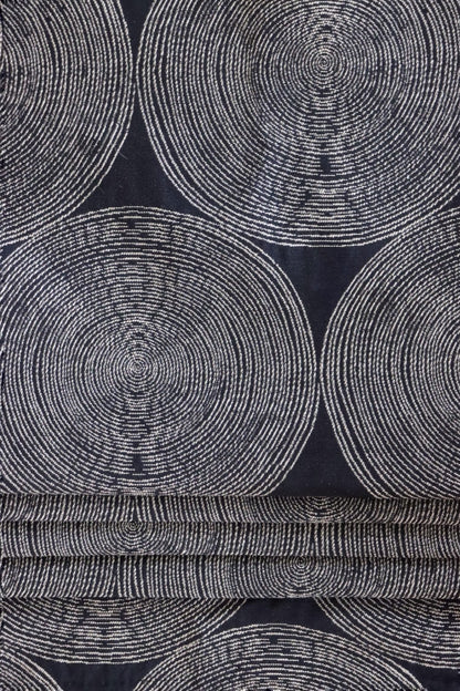 The Adam Black fabric by Arte Fresca Outlet arranged in neat folds, mimicking a roller blind, showcasing its crisp lines and how the striking pattern of light circles on a dark black woven background creates a bold, modern statement.