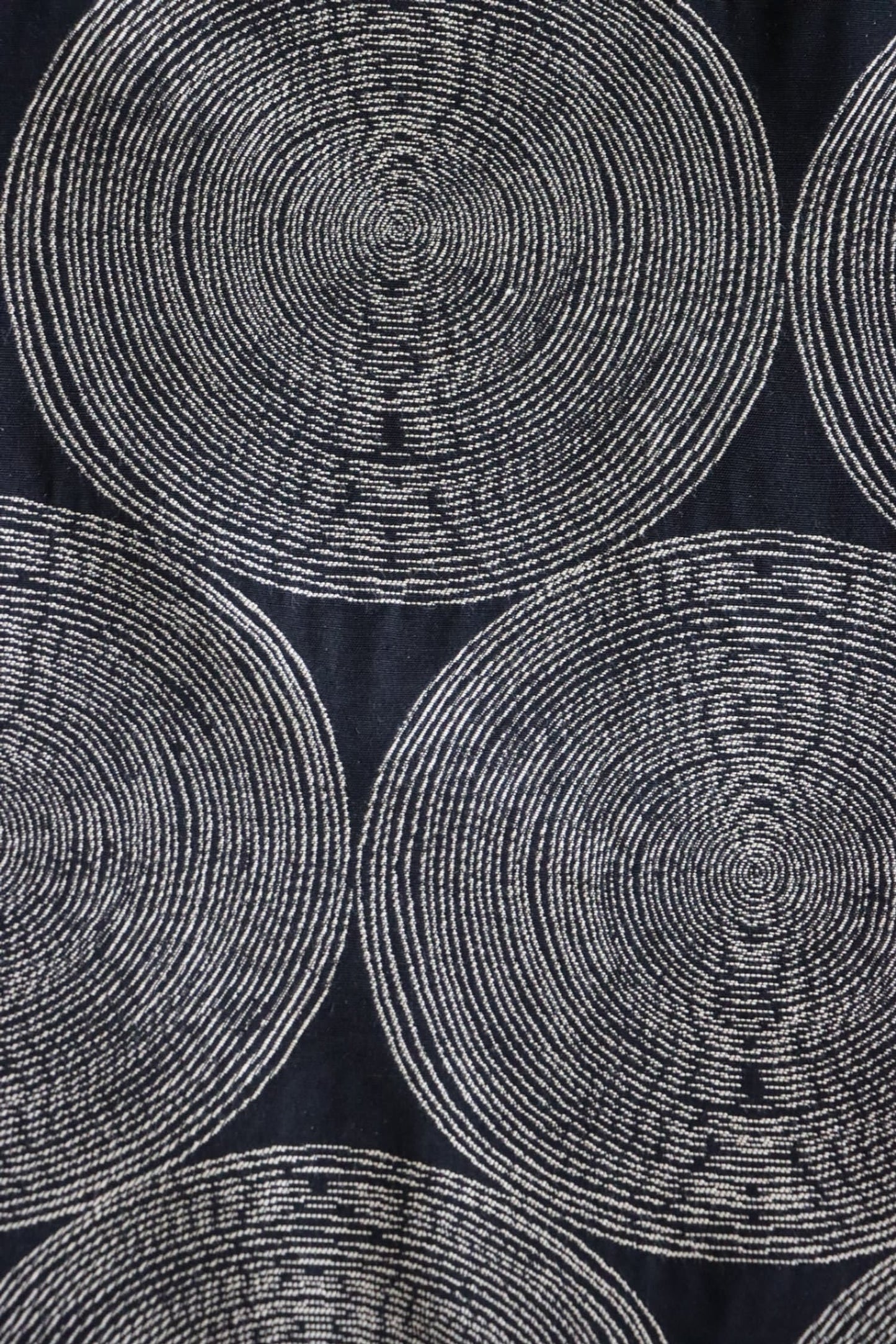   Detailed close-up of the Adam Black fabric from Arte Fresca Outlet, highlighting the intricate woven texture and the subtle color variations within the cream and beige concentric circles against the rich, almost night-black background.