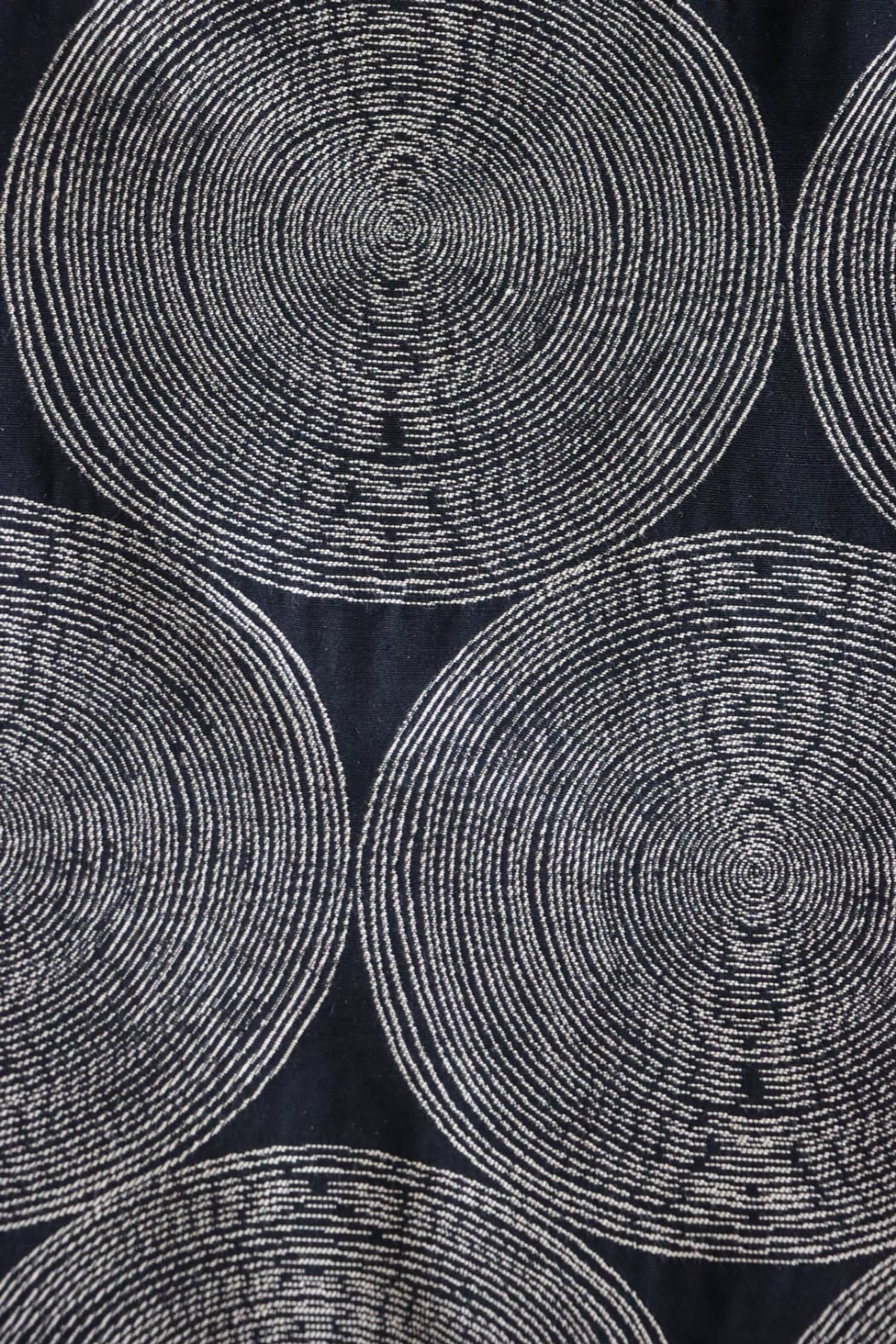   Detailed close-up of the Adam Black fabric from Arte Fresca Outlet, highlighting the intricate woven texture and the subtle color variations within the cream and beige concentric circles against the rich, almost night-black background.