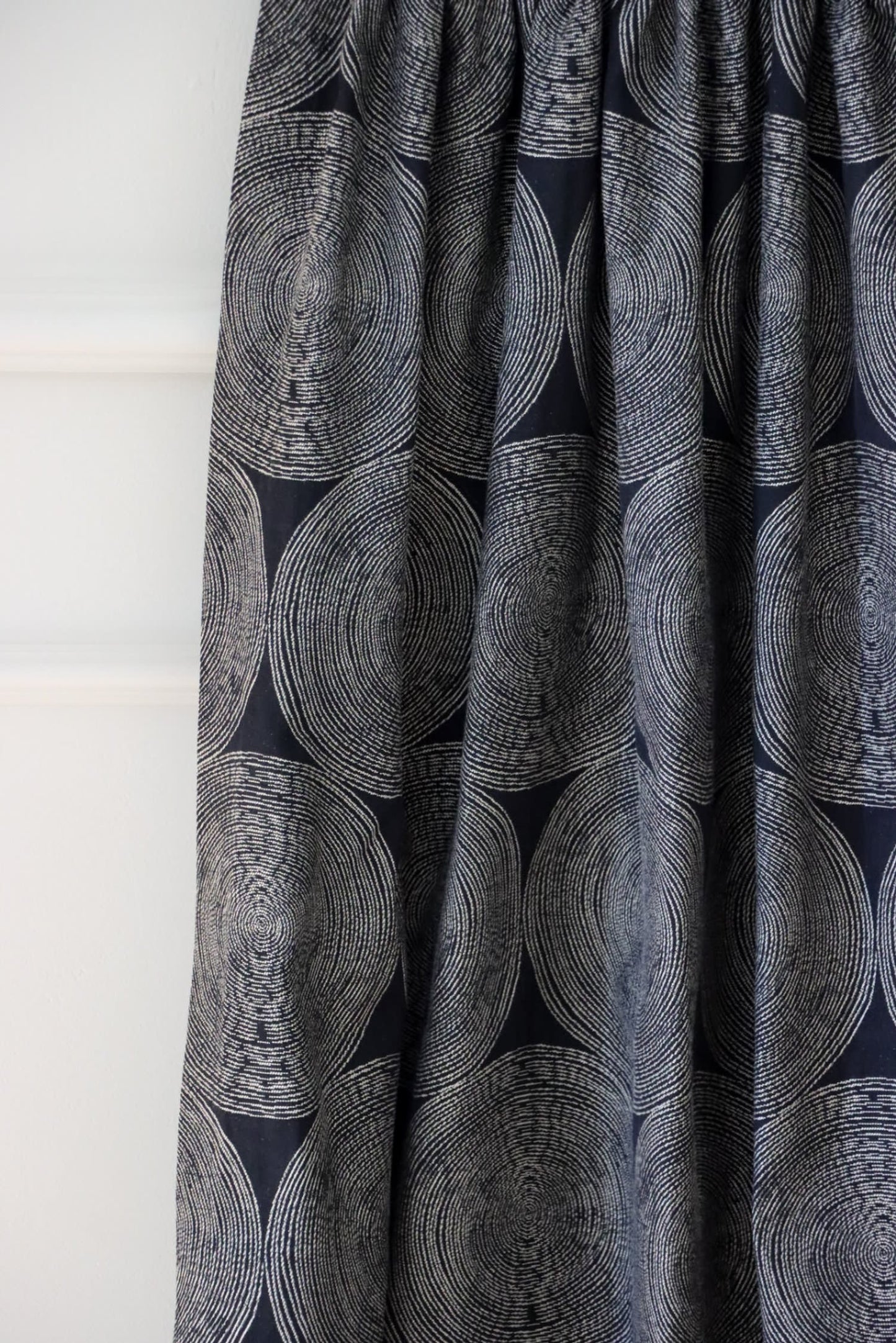 Adam Black fabric from Arte Fresca Outlet, folded to resemble a curtain, emphasizing its graceful drape and how the rhythmic pattern of cream and beige circles interacts with the folds on the deep black woven textile.