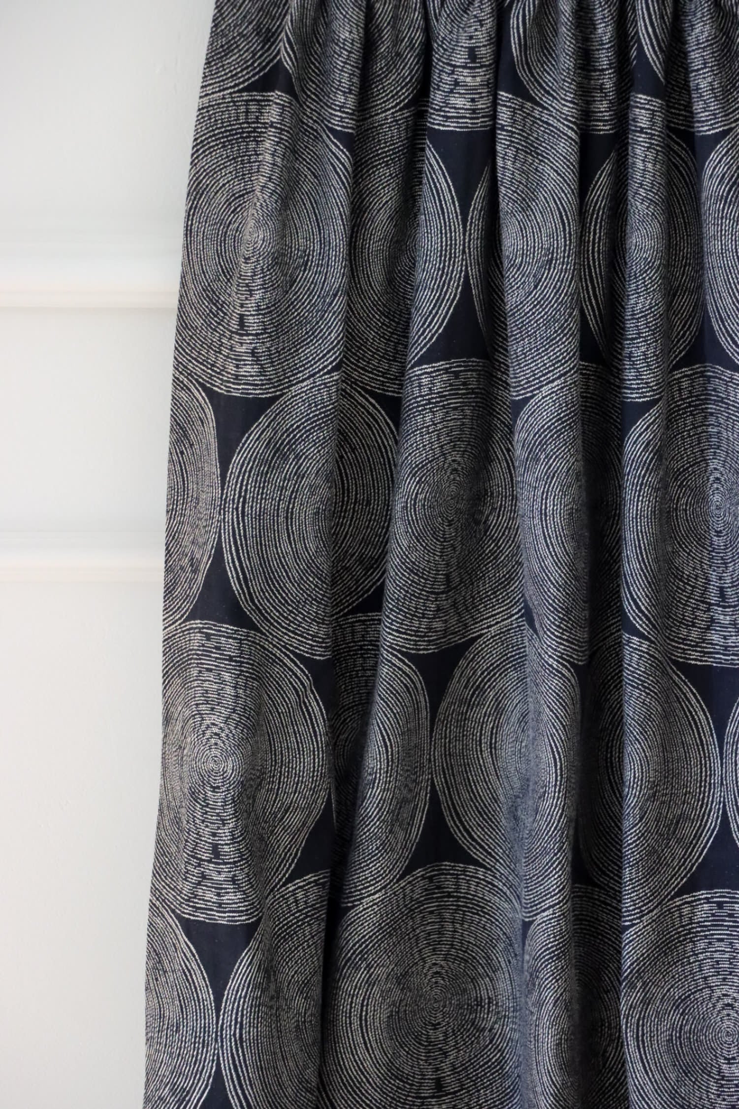 Adam Black fabric from Arte Fresca Outlet, folded to resemble a curtain, emphasizing its graceful drape and how the rhythmic pattern of cream and beige circles interacts with the folds on the deep black woven textile.