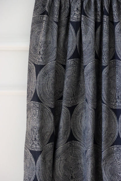 Adam Black fabric from Arte Fresca Outlet, folded to resemble a curtain, emphasizing its graceful drape and how the rhythmic pattern of cream and beige circles interacts with the folds on the deep black woven textile.