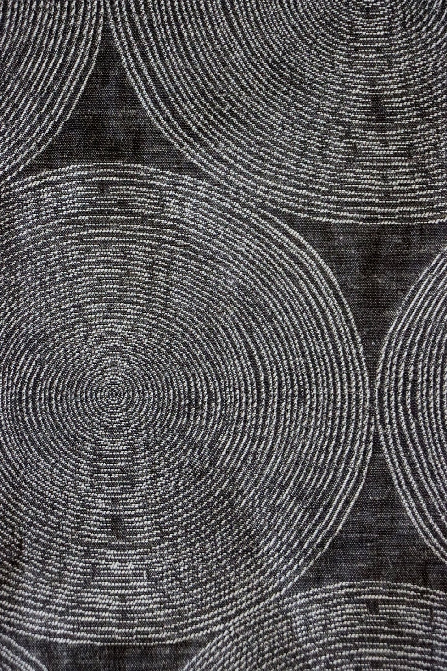 Close-up of ADAM CHARCOAL fabric from Arte Fresca Outlet, revealing the fine weave, the subtle texture within its concentric cream and silver-grey circles on deep anthracite, emphasizing its quality and sophisticated detail.