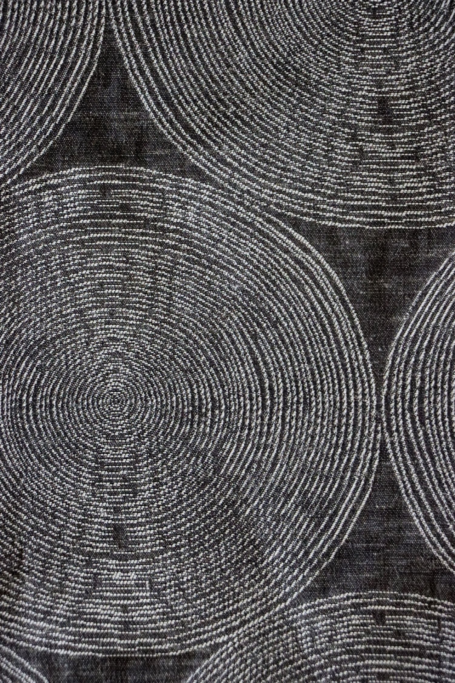 Close-up of ADAM CHARCOAL fabric from Arte Fresca Outlet, revealing the fine weave, the subtle texture within its concentric cream and silver-grey circles on deep anthracite, emphasizing its quality and sophisticated detail.