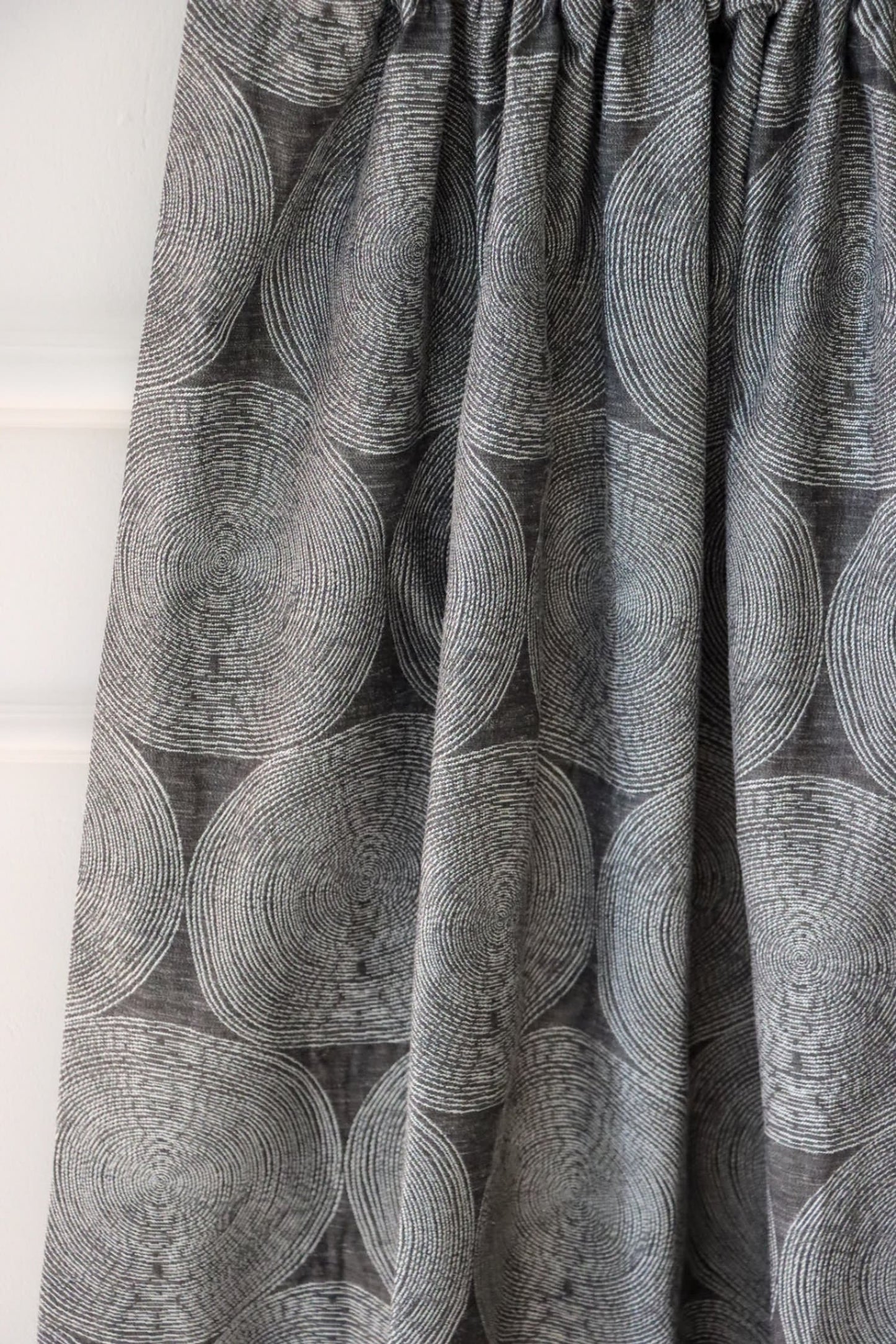 ADAM CHARCOAL fabric from Arte Fresca Outlet, elegantly folded in drapes like a curtain, showcasing its fluid quality, the subtle concentric circle pattern on deep anthracite, and its suitability for creating modern, serene window treatments.