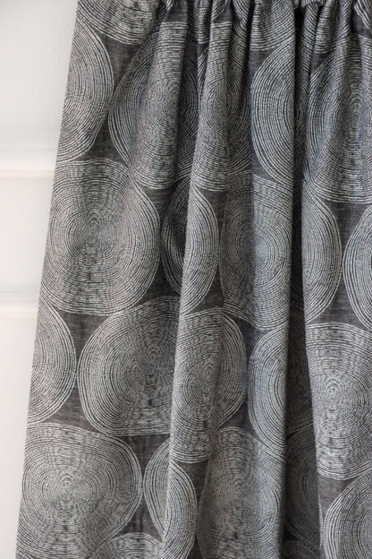 ADAM CHARCOAL fabric from Arte Fresca Outlet, elegantly folded in drapes like a curtain, showcasing its fluid quality, the subtle concentric circle pattern on deep anthracite, and its suitability for creating modern, serene window treatments.