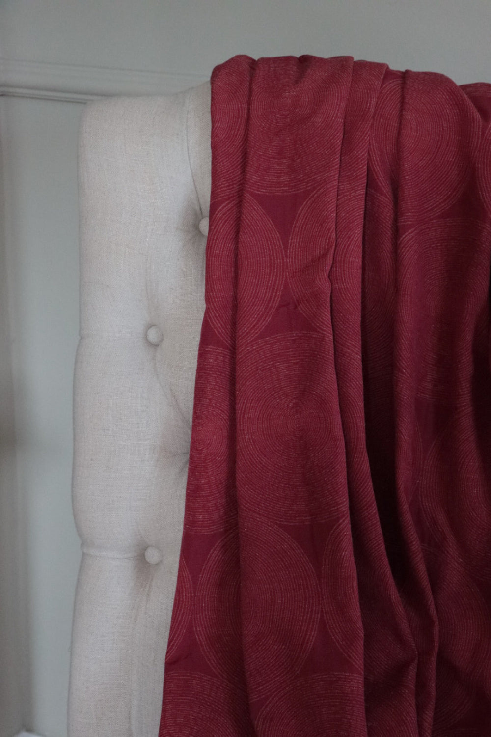 ADAM RED fabric by Arte Fresca Outlet draped loosely over a light upholstered chair back, illustrating the scale of its geometric concentric circle pattern in deep red, ideal for assessing design repeat and how it flows.