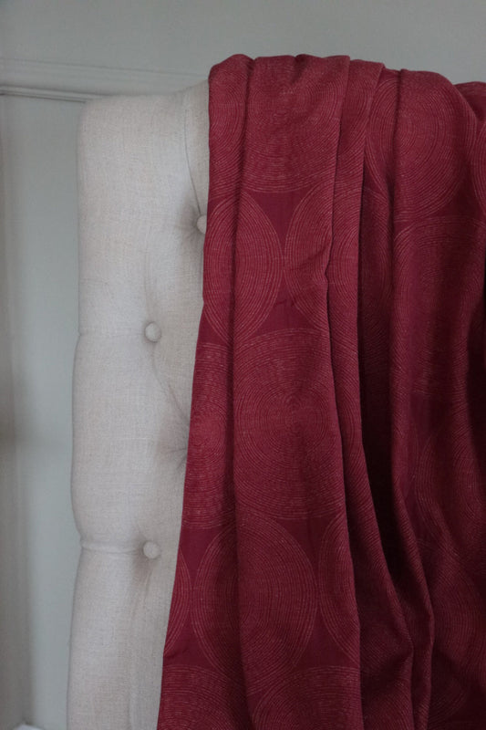 ADAM RED fabric by Arte Fresca Outlet draped loosely over a light upholstered chair back, illustrating the scale of its geometric concentric circle pattern in deep red, ideal for assessing design repeat and how it flows.