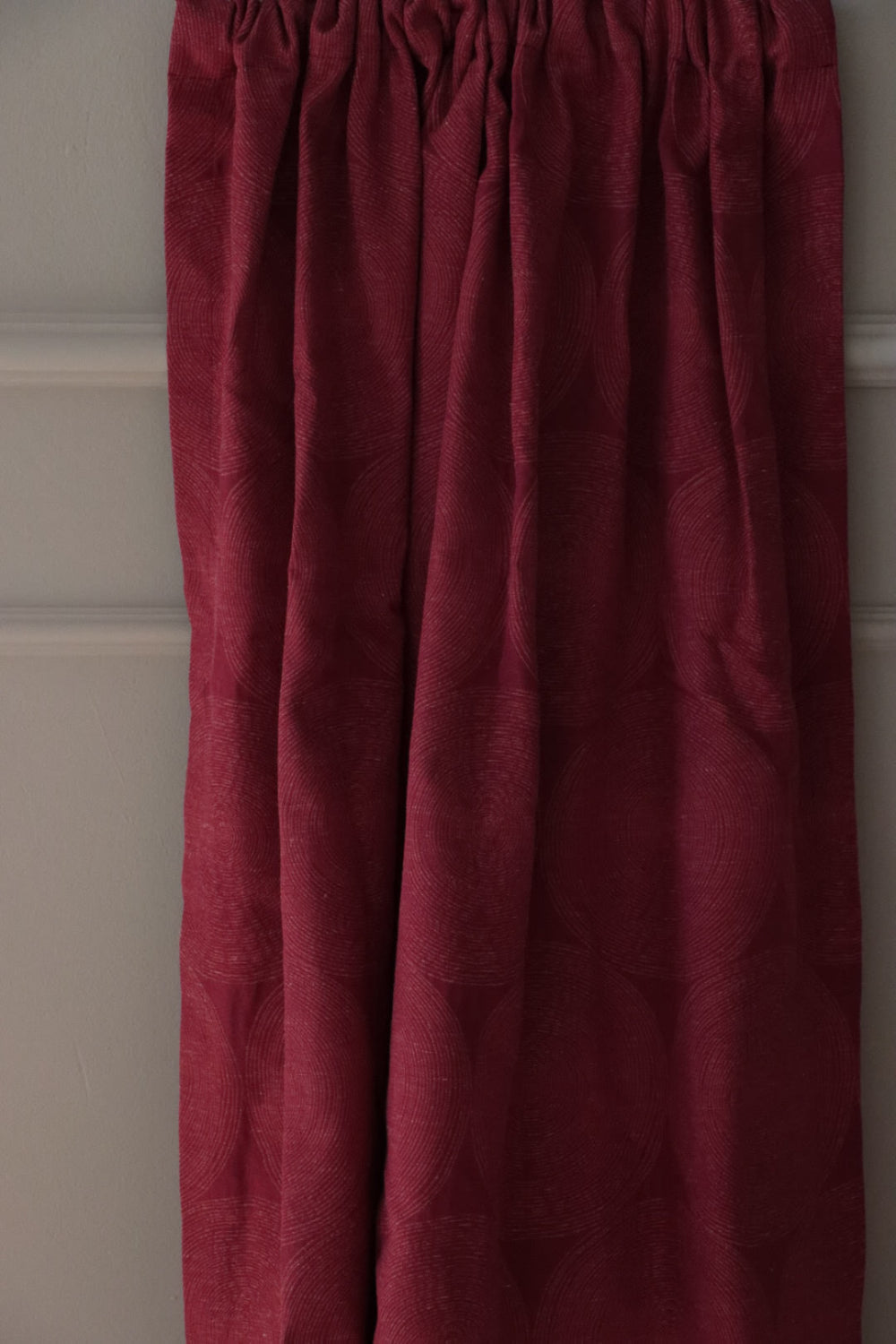 ADAM RED fabric from Arte Fresca Outlet, elegantly folded in drapes like a curtain, showcasing its luxurious fall, the rich burgundy red geometric pattern, and its suitability for creating dramatic and warm window treatments.