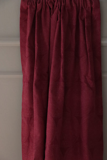 ADAM RED fabric from Arte Fresca Outlet, elegantly folded in drapes like a curtain, showcasing its luxurious fall, the rich burgundy red geometric pattern, and its suitability for creating dramatic and warm window treatments.
