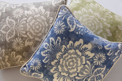 Three decorative throw pillows with ornate floral damask patterns, shown in blue, beige, and sage green, with the blue pillow in the foreground.