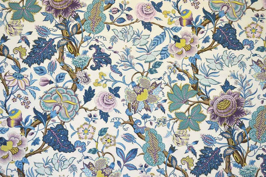 A close-up of a fabric pattern featuring a dense botanical design with blue, purple, pink, and yellow flowers, leaves, and birds on a cream background.