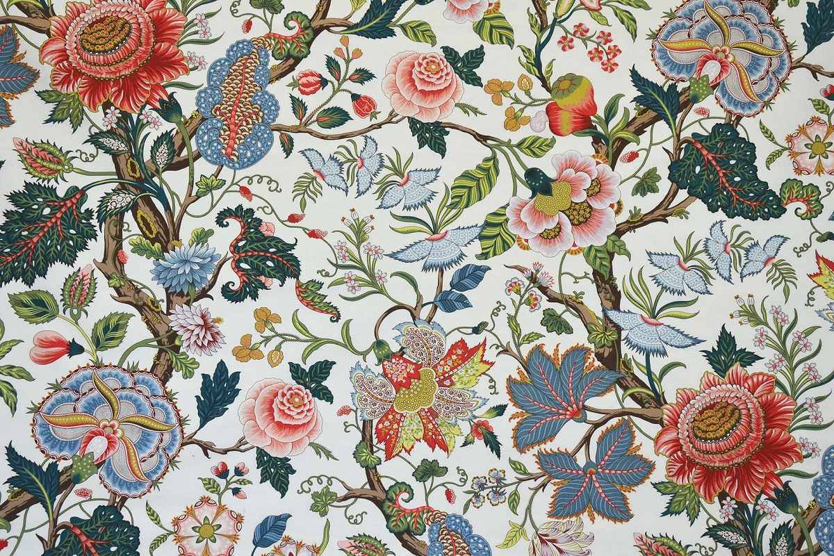 A close-up of a classic toile patterned fabric featuring red, pink, blue, and green floral motifs on a cream background.