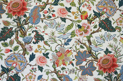 A close-up of a classic toile patterned fabric featuring red, pink, blue, and green floral motifs on a cream background.