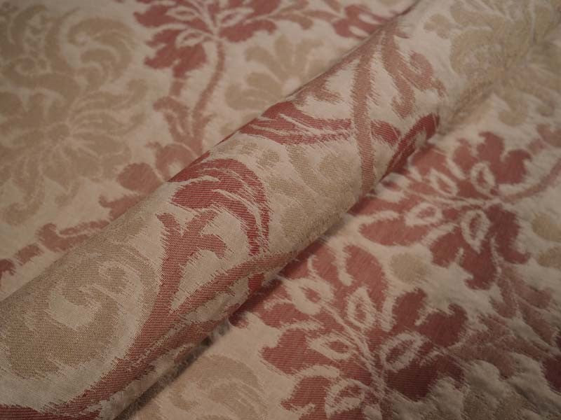 A close-up of a damask patterned fabric with a beige background and a rust-red floral motif, folded to show its texture.
