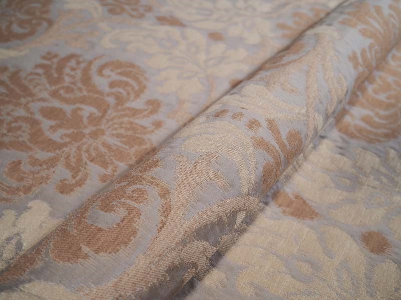 A close-up of a beige and brown damask patterned fabric, showing its texture and weave.