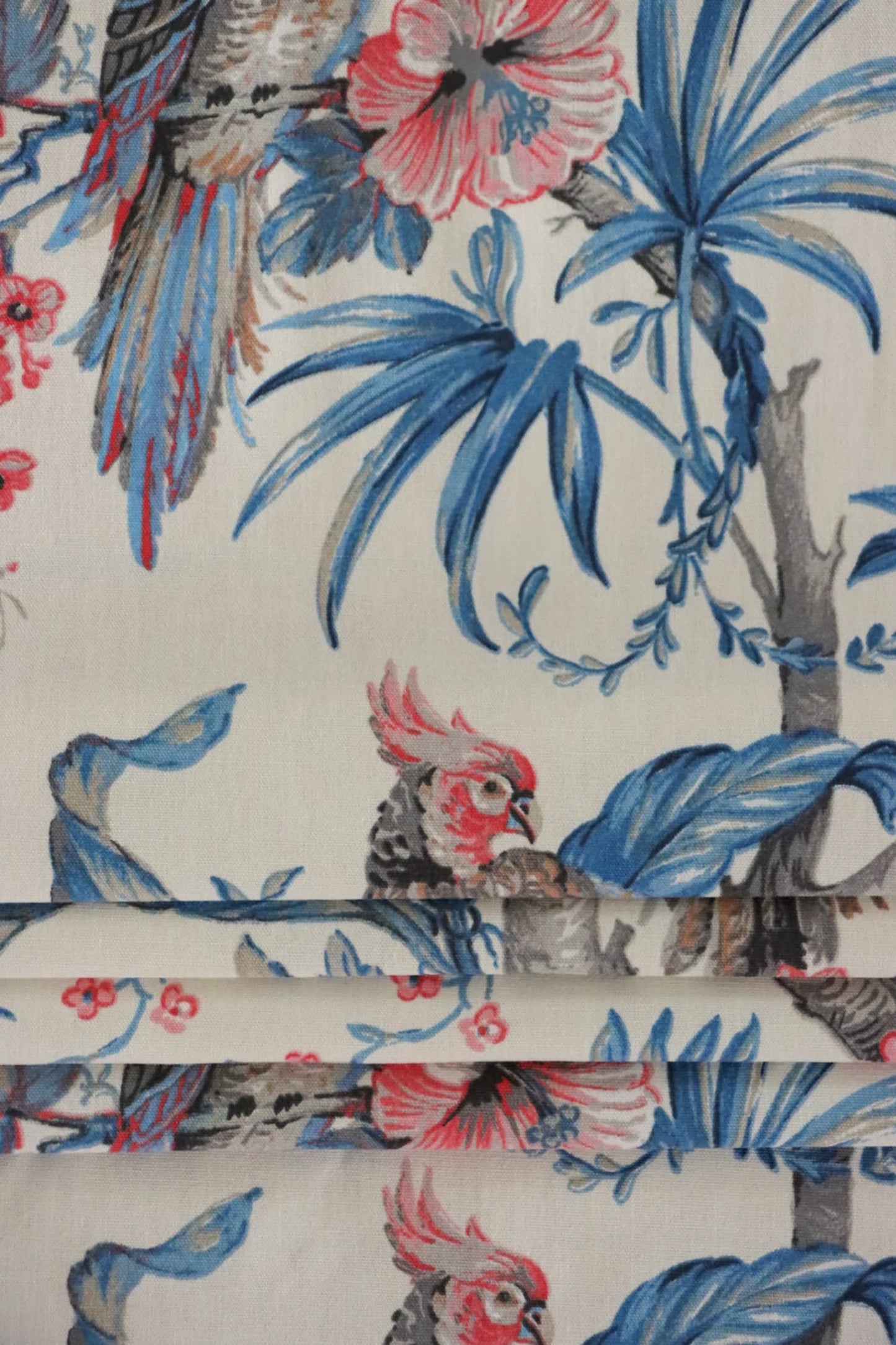 Allegria Blue/Cream fabric by Arte Fresca Outlet folded like a Roman blind, illustrating its structured appearance and the exotic tropical design with the parrot and hibiscus pattern, perfect for window treatments.