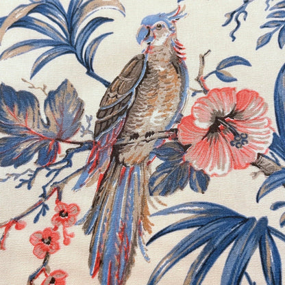 Close-up of ALLEGRIA BLUE/CREAM fabric coupon from Arte Fresca Outlet, showcasing the intricate details of the tropical pattern. A colorful parrot, hibiscus flowers, and leaves are depicted with fine lines and careful drawing in blue, red, and beige on a cream 100% cotton textile, highlighting its exquisite quality.
