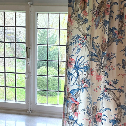 ALLEGRIA BLUE/CREAM fabric coupon by Arte Fresca Outlet folded to demonstrate its drape, showing the tropical parrot and hibiscus pattern in blue, red, and beige on cream cotton. This remnant piece, ideal for decorative uses, displays its light and flowing quality.