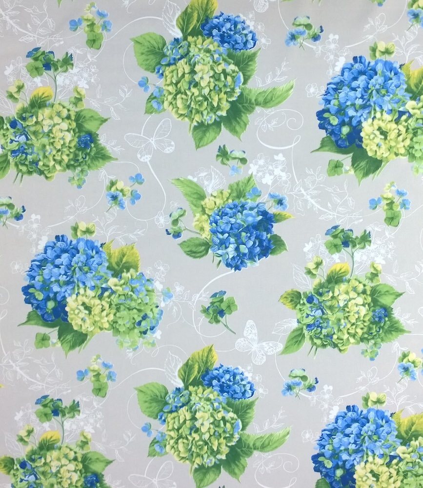 A close-up of a floral fabric pattern featuring blue and green hydrangea bouquets with white butterfly and scroll motifs on a light gray background.