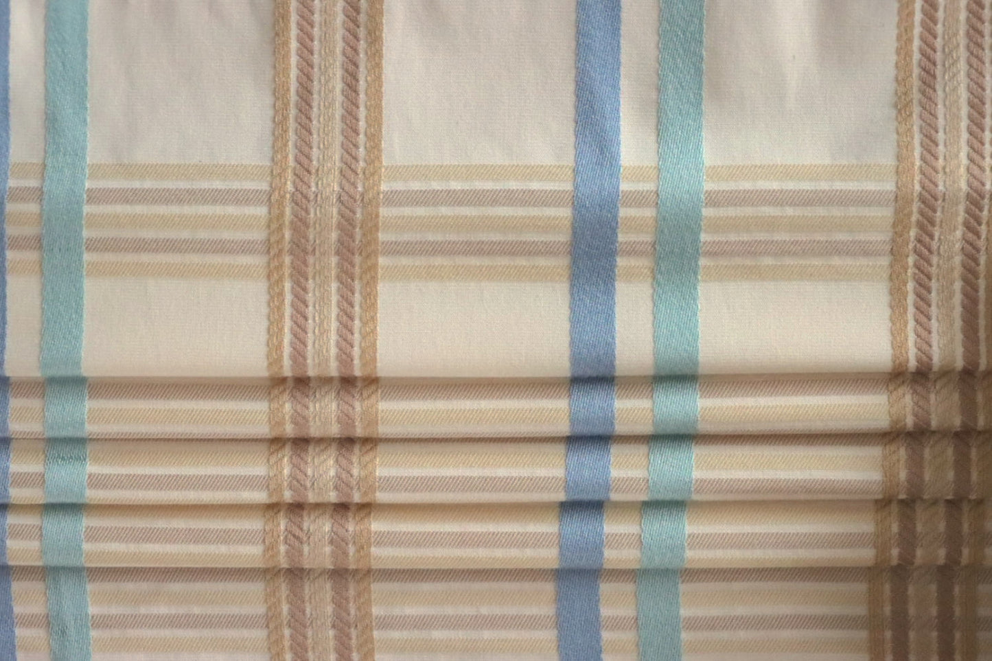 BRAXTON CHECK BLUE/CREAM fabric by Arte Fresca Outlet, folded precisely like a Roman blind, highlighting its structured yet soft nature, the clean lines of the blue, cream, and brown check, and its suitability for elegant blind designs.