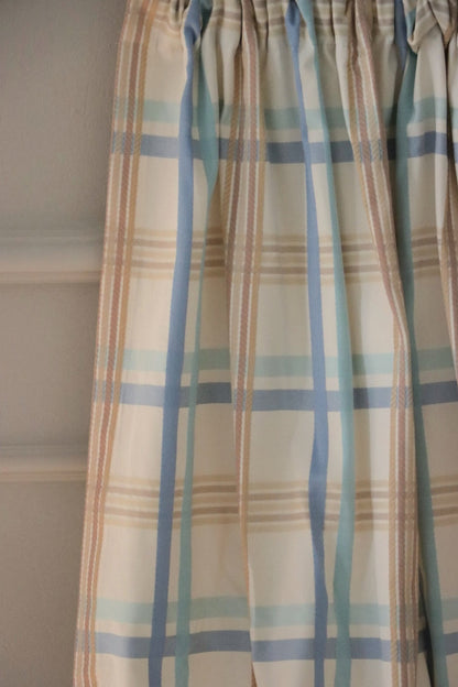 BRAXTON CHECK BLUE/CREAM fabric from Arte Fresca Outlet, elegantly folded in drapes like a curtain, showcasing its soft fall, the harmonious blue, cream, and brown check pattern, and its suitability for stylish window treatments.