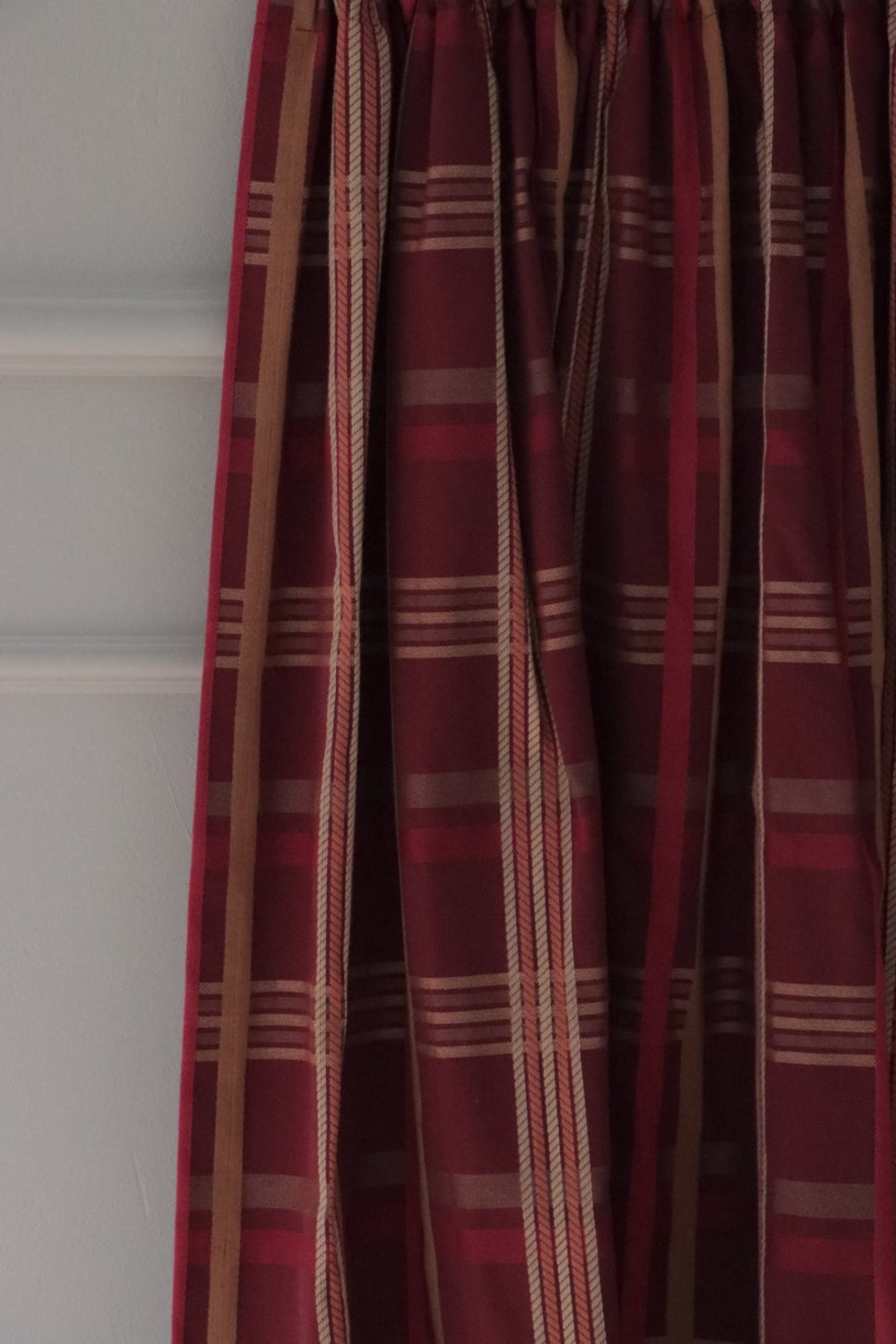Braxton Check Burgundy fabric by Arte Fresca Outlet elegantly folded, demonstrating its beautiful drape and suitability as a curtain fabric, revealing the sophisticated plaid in burgundy, gold, and beige.