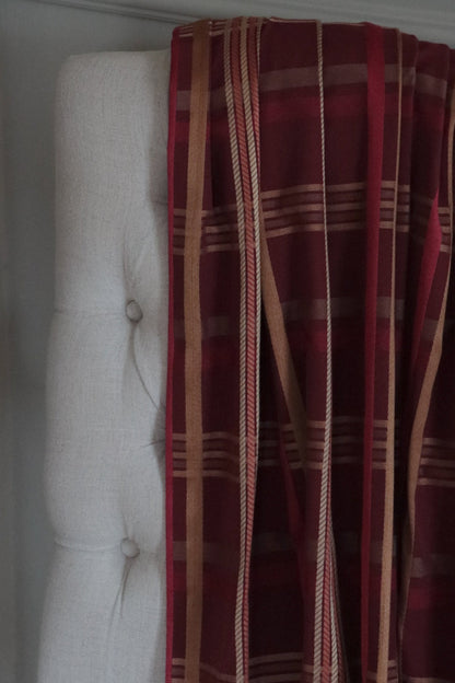 Braxton Check Burgundy fabric by Arte Fresca Outlet draped loosely over a light upholstered chair back, showcasing the scale of its elegant plaid pattern in warm burgundy, golden, and rosé hues.