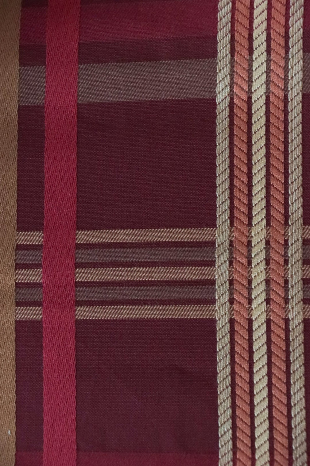 Close-up of Braxton Check Burgundy fabric by Arte Fresca Outlet, detailing the rich woven texture and the intricate plaid pattern with varied stripe widths and subtle rope-like lines in burgundy, gold, and pink.
