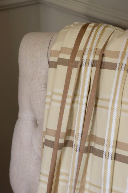 Braxton Check fabric draped loosely over a light upholstered chair, showing the scale of the classic beige and brown plaid pattern from Arte Fresca Outlet.