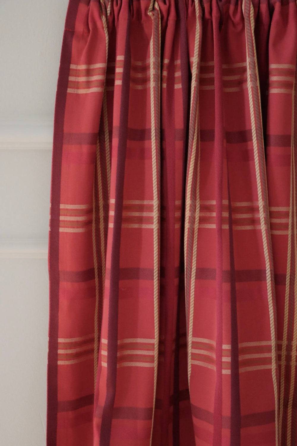 BRAXTON CHECK RASPBERRY fabric from ARTE FRESCA Outlet elegantly folded, resembling a curtain. This image demonstrates the fabric's beautiful drape and how its vibrant check pattern enhances light and adds warmth to a room.