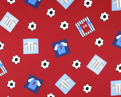 Red fabric with a repeating soccer-themed pattern featuring blue and light blue jerseys, striped shirts, soccer balls, and number patches.