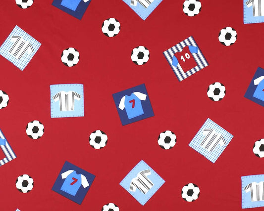 Red fabric with a repeating soccer-themed pattern featuring blue and light blue jerseys, striped shirts, soccer balls, and number patches.