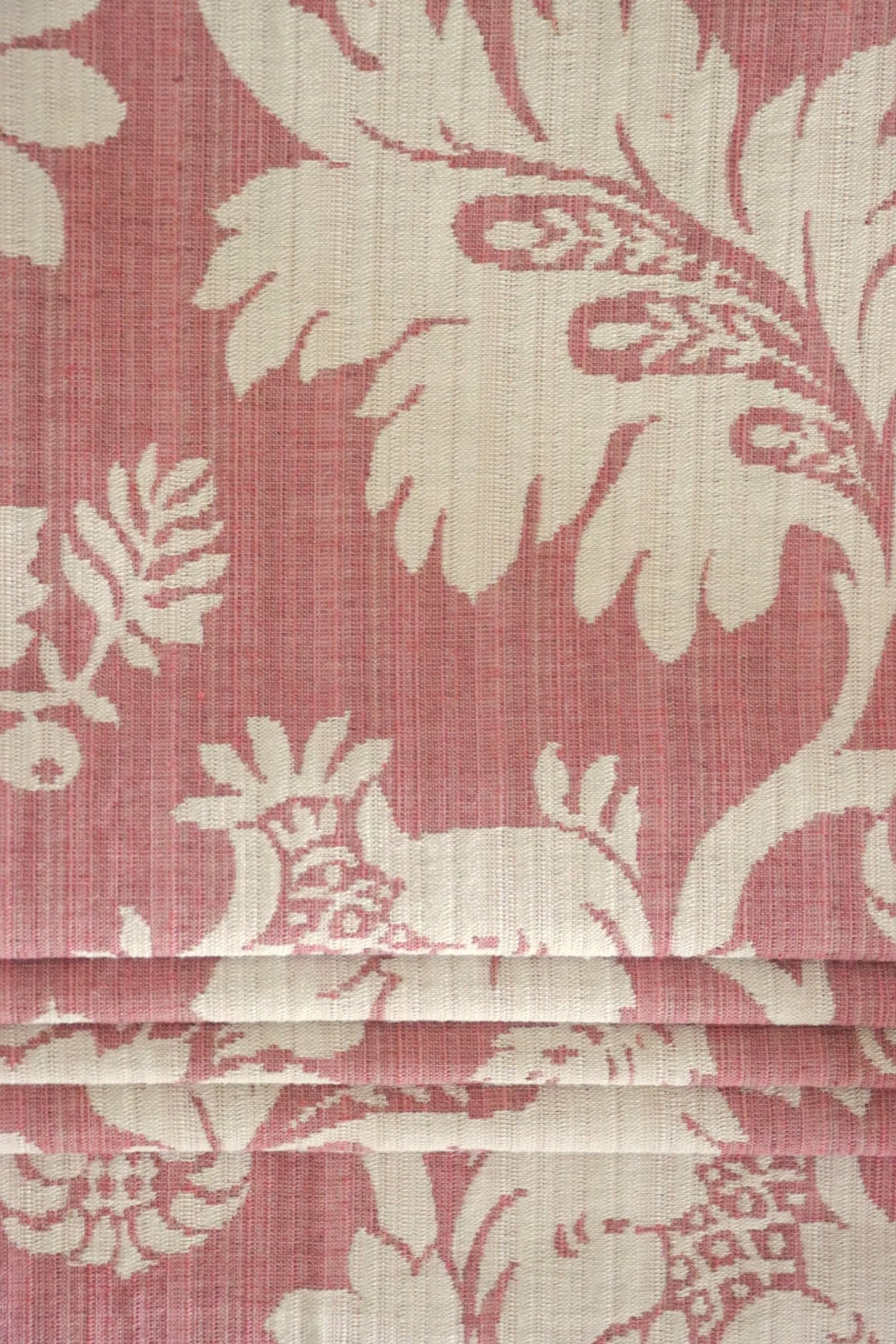  MARY ROSE jacquard fabric from Arte Fresca Outlet folded compactly like a window blind, emphasizing its refined woven texture and the prominent creamy white floral pattern on old rose. This versatile jacquard is suitable for elegant roller blinds and decorative projects, offering a touch of classic, romantic beauty.