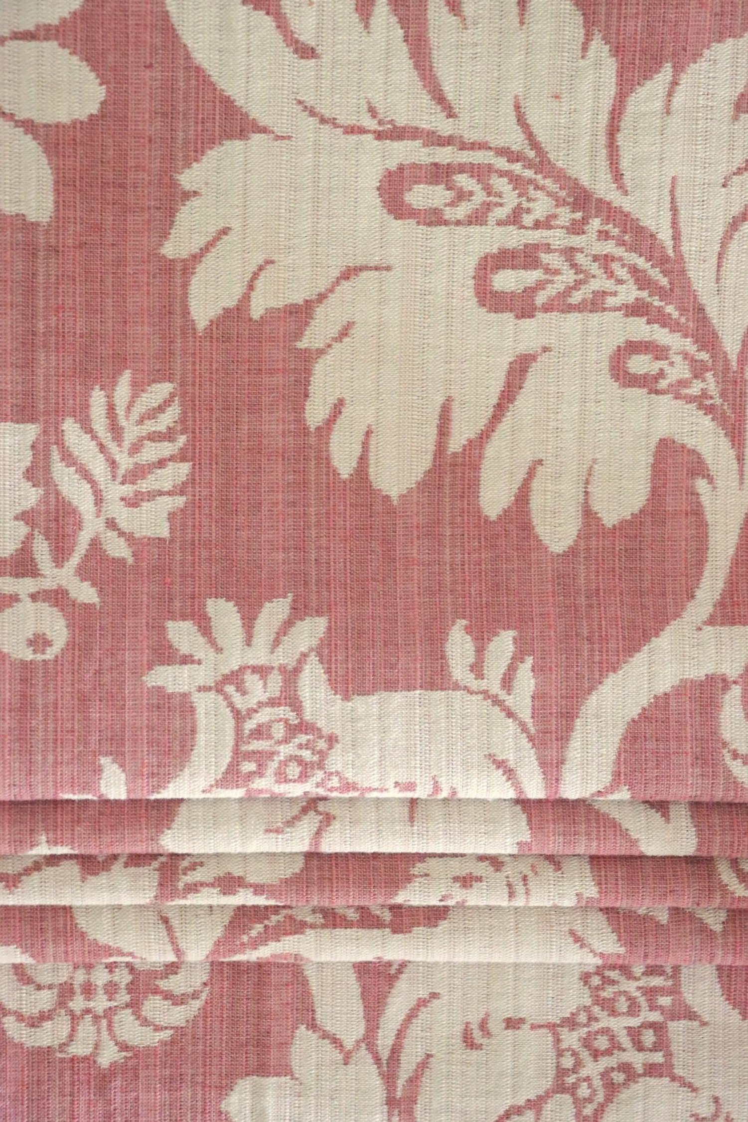  MARY ROSE jacquard fabric from Arte Fresca Outlet folded compactly like a window blind, emphasizing its refined woven texture and the prominent creamy white floral pattern on old rose. This versatile jacquard is suitable for elegant roller blinds and decorative projects, offering a touch of classic, romantic beauty.