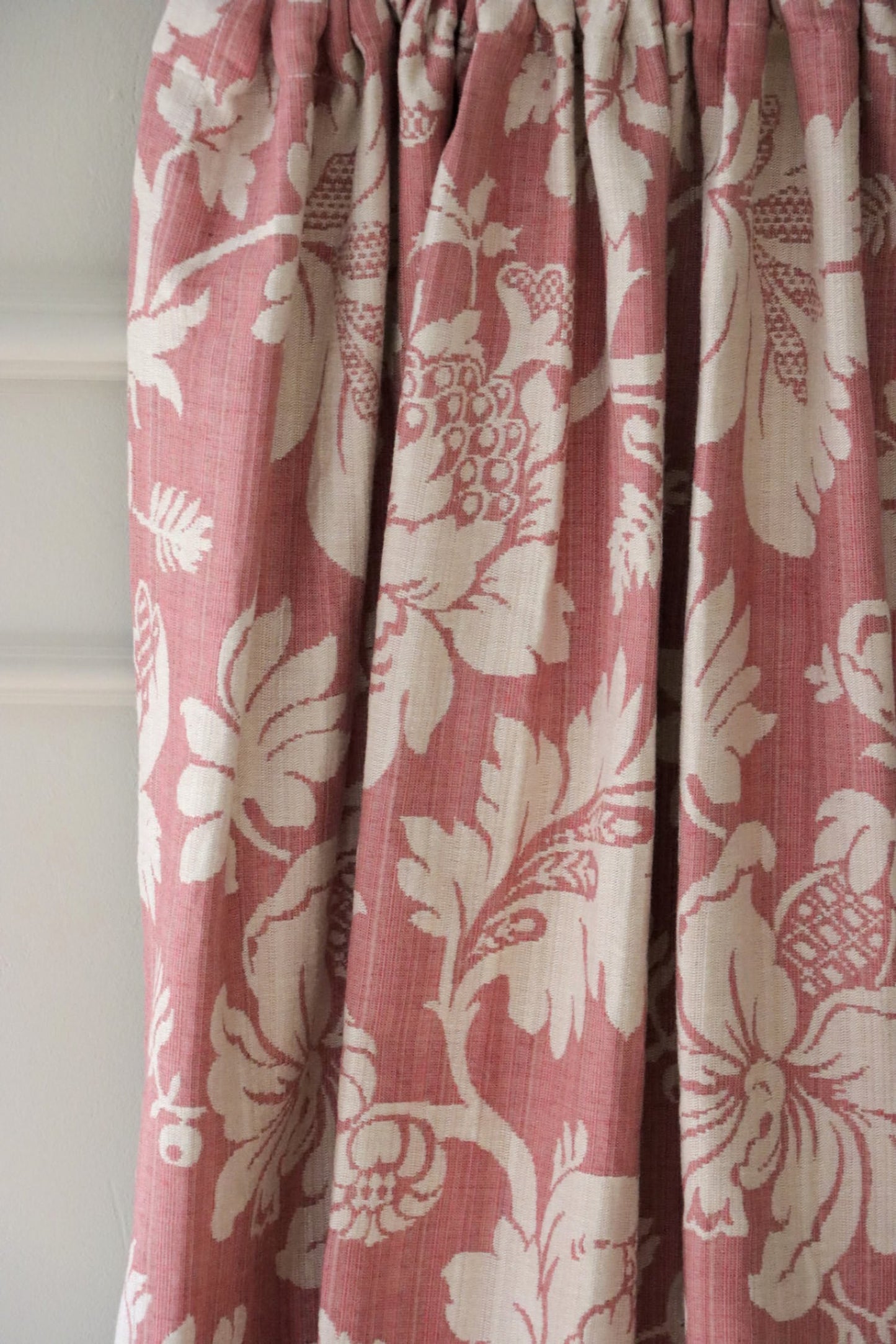 MARY ROSE jacquard fabric by Arte Fresca Outlet gracefully folded like curtain material, highlighting its soft drape and the elegant, woven floral pattern. The creamy white blossoms on a soft old rose background create a romantic, timeless ambiance for window treatments, filtering light beautifully.