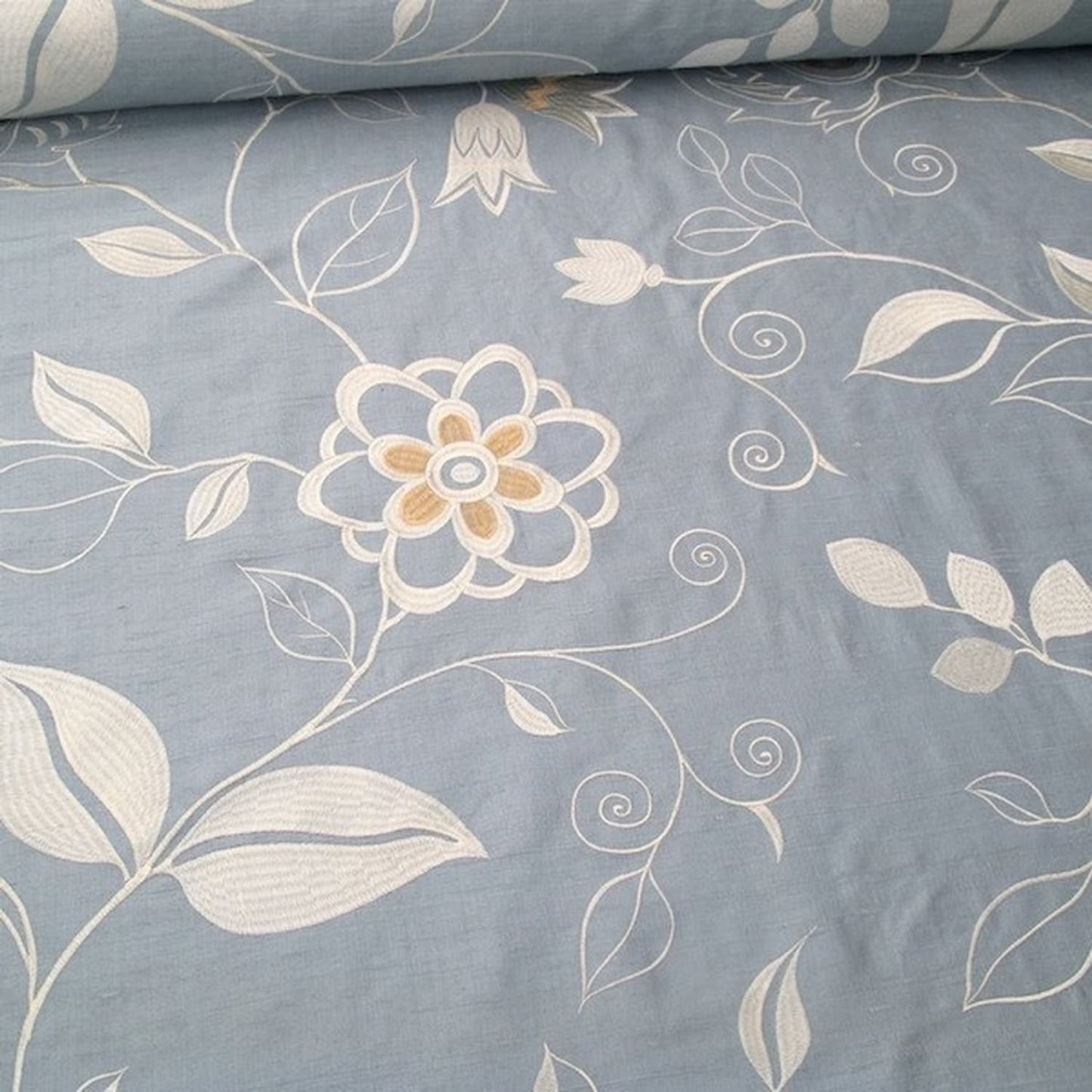 Close-up of MOREEN AQUA embroidered silk fabric from Arte Fresca Outlet, revealing the raised, intricate floral embroidery. Silvery ivory and creamy beige threads form decorative blossoms and swirling stems on the smooth, shimmering aqua light-blue silk-rayon ground, showcasing its delicate artistry and luxurious texture.