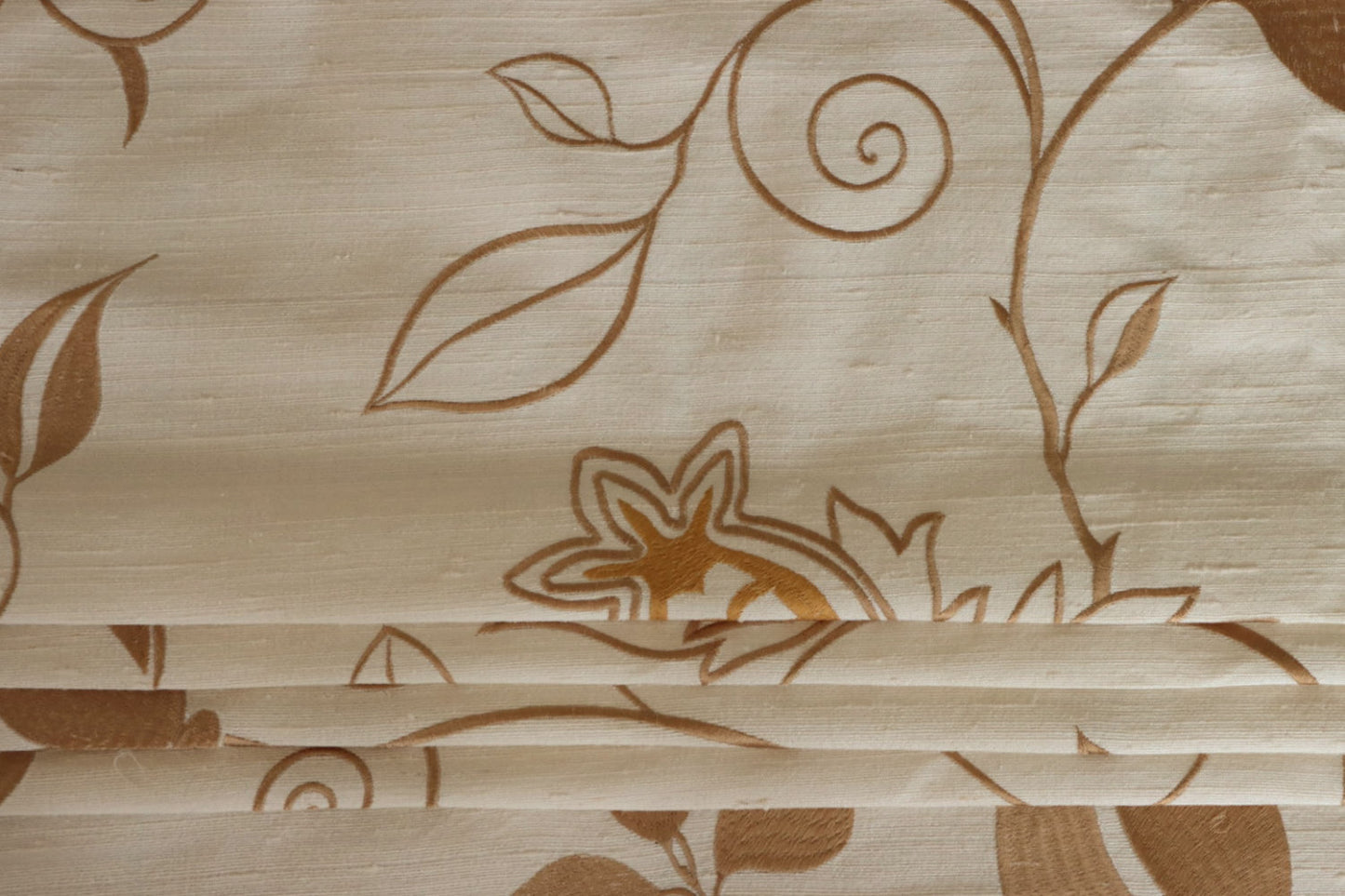 MOREEN CAMEL silk fabric by Arte Fresca Outlet, folded precisely like a Roman blind, highlighting its structured yet soft nature, the clear definition of its embroidered floral pattern, and its ability to create sophisticated, richly textured window coverings.