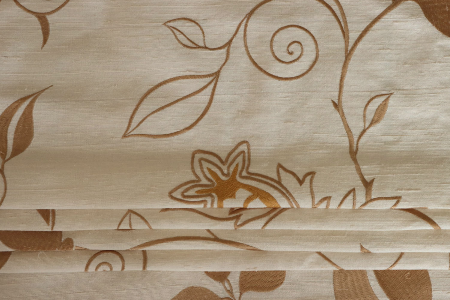 MOREEN CAMEL silk fabric by Arte Fresca Outlet, folded precisely like a Roman blind, highlighting its structured yet soft nature, the clear definition of its embroidered floral pattern, and its ability to create sophisticated, richly textured window coverings.